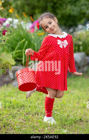 Schönes tanzendes Mädchen mit einer roten Geschenkbox in einem roten Kleid mit Polka im Sommergarten Stockfoto