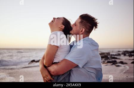Sonnenuntergang, Liebe und junges Paar am Strand, lachen und genießen ihre Flitterwochen. Glücklich, lustig und Mann umarmt und spielt mit Frau Stockfoto