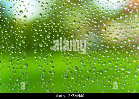 Regentropfen auf dem Glasfenster auf einem grünen Hintergrund im Freien Stockfoto