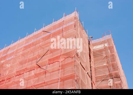 Die im Bau befindliche Gebäudefassadenecke ist mit einem schützenden Konstruktionsnetz abgedeckt. Gebäude im Bau mit rosa Schutz saf verpackt Stockfoto