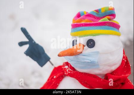 Schneemann in einem Regenbogenhut und einer medizinischen Maske. Stockfoto