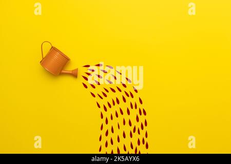 Eine orangefarbene Gießkanne mit einem abstrakten Wasserstrom aus roten Blütenblättern auf gelbem Hintergrund Stockfoto