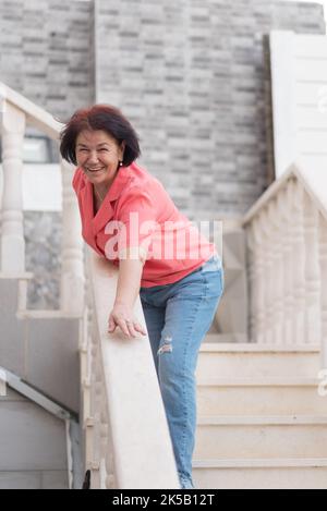 Glückliche optimistische ältere Frau, die sich draußen auf Treppengeländer stützt. Stockfoto