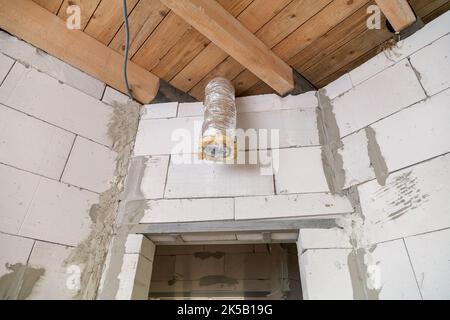 Installation einer Rohrheizung. Heizen zu Hause mit heißer Luft. Verlegung und Befestigung isolierter Rohre an der Decke. Stockfoto