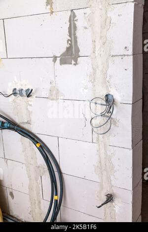 Hintergrund des elektrischen Verdrahtungskonzepts. Der Elektrokasten mit Drähten ist an einer weißen Wand montiert. Baustelle im Innenbereich Stockfoto