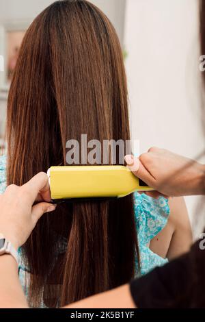 Hände eines Friseurs. Der Meister gleicht die Haare des Kunden mit einem Lockenstab aus Stockfoto