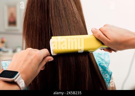 Hände eines Friseurs. Der Meister gleicht die Haare des Kunden mit einem Lockenstab aus Stockfoto