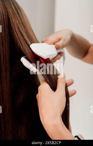 Hände eines Friseurs. Der Meister gleicht die Haare des Kunden mit einem Lockenstab aus Stockfoto