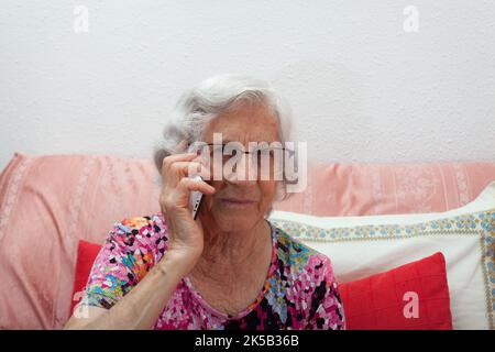 Ältere Frau, die zu Hause vom Sofa aus telefoniert, Einsamkeit der älteren Menschen, Technologie bei älteren Menschen. Stockfoto
