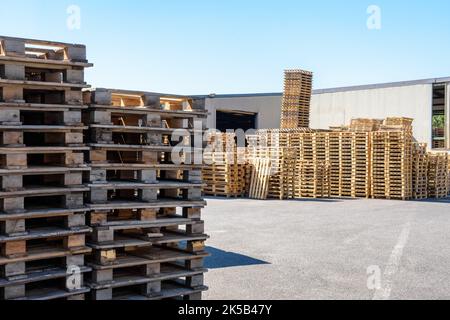 Neue und gebrauchte Holzpaletten, die an einem sonnigen Tag im Innenhof eines Lagerhauses gestapelt wurden. Stockfoto