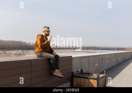 Bärtiger Mann, der in der Frühlingspromenade einen Shake trinkt. Getränke zum Mitnehmen und Gen z oder Millennial Youth Konzept. Platz für Werbung kopieren Stockfoto