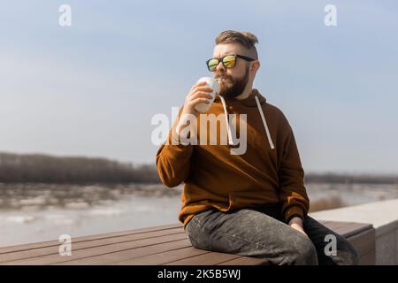 Bärtiger Mann, der in der Frühlingspromenade einen Shake trinkt. Getränke zum Mitnehmen und Gen z oder Millennial Youth Konzept. Platz für Werbung kopieren Stockfoto