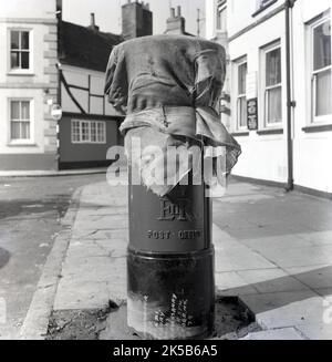 1964, historisch, auf einem Bürgersteig, eine neu errichtete Säule oder ein Briefkasten, der mit alten Postsäcken bedeckt war, noch nicht in Gebrauch, da seine Betonbasis aufgestellt werden musste, Aylesbury, England, Großbritannien. Stockfoto