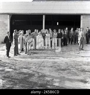 1964, historisch, Gruppe von Männern und Frauen auf einem Bauernhof bei einem Besuch auf Manor Farm, Haddenham, Aylesbury, Bucks, England, Großbritannien, mit einem Gentleman, der einen Lautsprecher verwendet, um mit erwachsenen Besuchern zu kommunizieren. Stockfoto