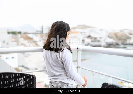 Kleines Mädchen, das auf dem Balkon mit Blick auf das Meer steht Stockfoto