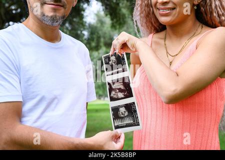 Ein Paar, das Ultraschall im Freien hält und eine Schwangerschaft ankündigt Stockfoto