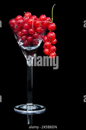 Rote Johannisbeeren in Cocktailglas auf schwarzem Hintergrund Stockfoto