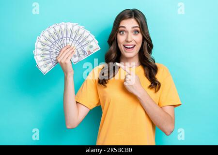 Foto von jungen aufgeregt funky ziemlich wunderschöne Mädchen welliges Haar Finger zeigen unerwartete Emotionen halten viel Geld reich lustig isoliert auf cyan Farbe Stockfoto