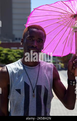 Mann in Kapstadt Holding Pink Sonnenschirm - Südafrika Stockfoto