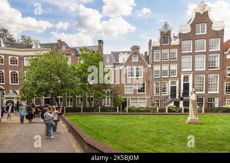 Touristen besuchen die alten historischen Häuser im Begijnhof, einem der ältesten Höfe Amsterdams. Stockfoto