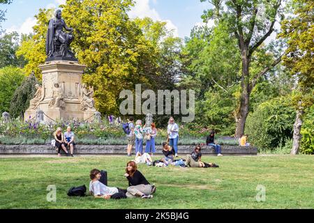 Junge Leute sitzen auf dem Rasen und genießen gemeinsam das schöne sonnige Wetter im Vondelpark in Amsterdam. Stockfoto