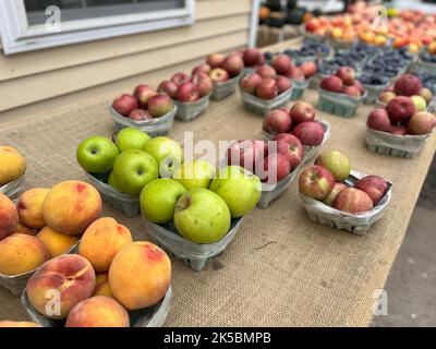 Körbe mit frisch gepflückten Pfirsichen und Äpfeln, die im Herbst an einem Farmstand am Straßenrand in New York verkauft werden. Stockfoto