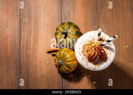Hausgemachter, beladen Kürbis-Gewürz-Milchshake mit Eis und herber Krümel, in einem Glas mit kleinen Kürbissen-Dekor, Pekannüssen und Gewürzen, gesund f Stockfoto