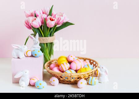 Ostern und Frühlingsferien Grußkartenkonzept. Rosa Tulpen, osterhasen mit bunten Eiern im Korb. Bemalte Ostereier im Nest und Tulpen mit Stockfoto