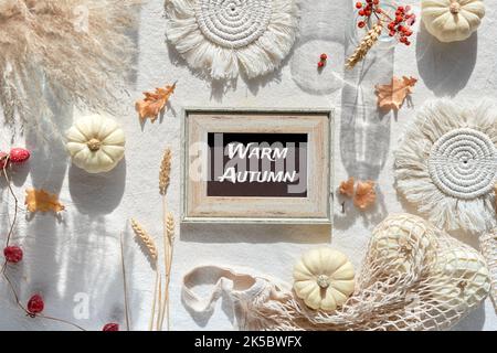 Aus weißem Textilhintergrund mit natürlichen Herbstdekorationen. Text Herbstliche Segnungen auf dem Briefbrett. Flach liegend, Draufsicht. Kürbisse im Netzbeutel, trockene Blätter Stockfoto