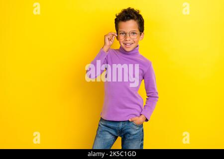 Foto von positiven Schulkind Hand berühren Brille strahlend Lächeln isoliert auf gelbem Hintergrund Stockfoto