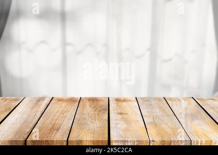 Leere Holztischplatte auf den verschwommenen Vorhängen um das Fenster. Für die Montage der Produktanzeige oder das Design wichtiger visueller Layouts. Stockfoto