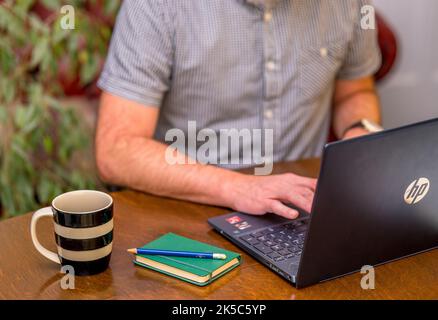 Mann, der an einem Schreibtisch sitzt und auf einem Laptop tippt Stockfoto