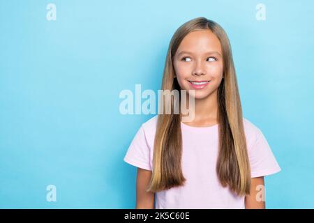 Foto von positiven optimistischen kleinen Mädchen mit geraden Frisur gekleidet rosa T-Shirt suchen leeren Raum auf blauem Hintergrund isoliert Stockfoto