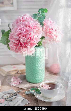 Komposition mit Teetasse und schönen rosa Blumen Hortensien in Vase, auf Holztisch, auf weißem Hintergrund Stockfoto