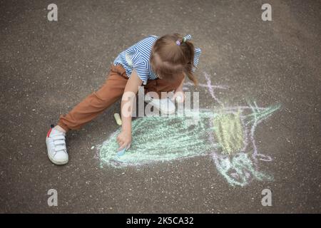 Kind zeichnet mit Kreide auf Asphalt. Stockfoto