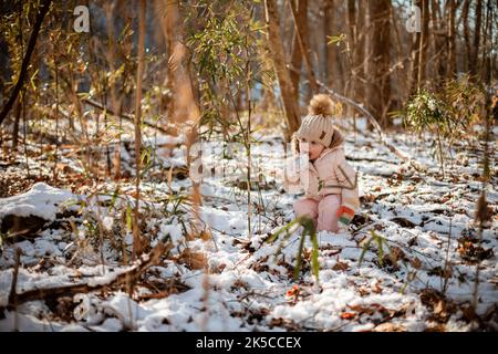 Kleines Kind im Winter, das draußen im Wald Schnee isst Stockfoto