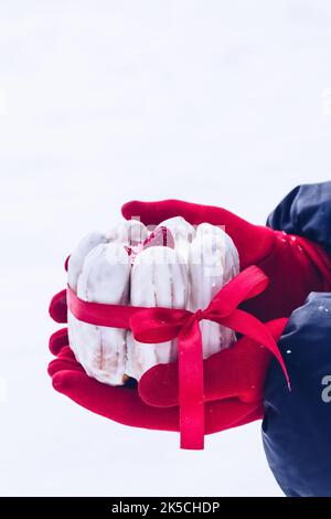 Weißer eclair (traditionelles französisches Dessert) Mini-Kuchen mit rotem Band. Eine Frau mit roten Handschuhen hält sich in den Händen. Freier Speicherplatz für Text Stockfoto