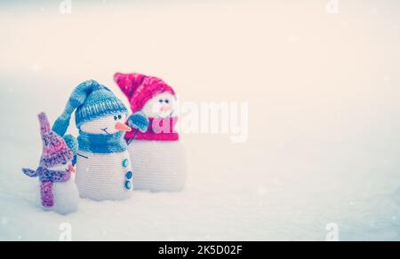 Kleine gestrickte Schneemänner auf dem weißen Schnee in der Natur. Stockfoto