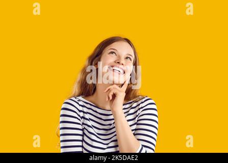 Die junge Frau lächelt und träumt davon, ihren Finger auf gelbem Hintergrund zu berühren. Stockfoto