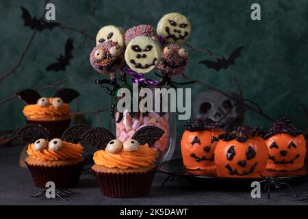 Vielfalt an Süßigkeiten Leckerbissen für Halloween - Helle Kuchen in Form von Fledermäusen, Kürbis-förmige Mousse Kuchen, Cake Pops Skelette und Monster mit Schokolade Stockfoto