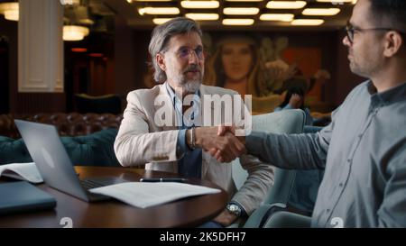 Serious Geschäftsmann macht Deal, Unterzeichnung Vertrag für eine erfolgreiche Partnerschaft. Geschäftstreffen im Bürorestaurant. Kooperationsvereinbarung der Unternehmen. Geschäftsleute geben sich die Hände Stockfoto