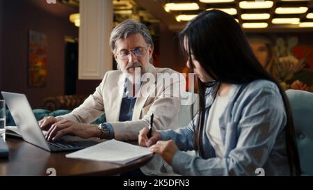 Asiatische Geschäftsfrau, die einen Vertrag unterzeichnet, um eine erfolgreiche Partnerschaft zu erreichen. Geschäftstreffen im Bürorestaurant. Kooperationsvereinbarung der Unternehmen. Geschäftsleute geben sich die Hände Stockfoto