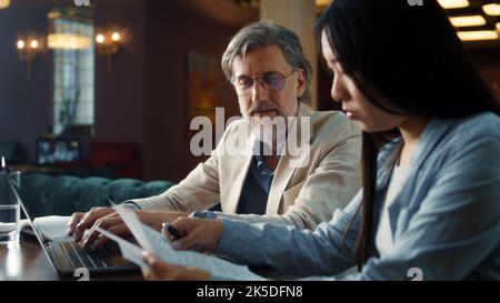 Asiatische Geschäftsfrau, die einen Vertrag unterzeichnet, um eine erfolgreiche Partnerschaft zu erreichen. Geschäftstreffen im Bürorestaurant. Kooperationsvereinbarung der Unternehmen. Geschäftsleute geben sich die Hände Stockfoto