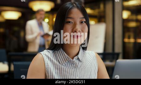 Asiatische Geschäftsfrau, die mit einem Laptop an der Kamera anschaut, an der Geschäftsstrategie oder dem Website-Design im modernen Büro arbeitet. E-Commerce-Unternehmen. Stockfoto