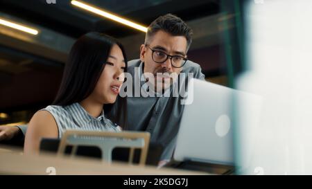 Asiatische Frau, die sich mit dem Vorgesetzten berät und die Geschäftsstrategie im modernen Büro mit einem Laptop und einem digitalen Tablet diskutiert. CEO des Marketingunternehmens mit einer Arbeitnehmerin Stockfoto