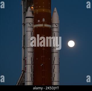 Der Mond steigt hinter der NASA-Rakete Space Launch System (SLS) mit der Orion-Sonde an Bord auf einem mobilen Trägerrakete auf, während er zum ersten Mal am Donnerstag, dem 17. März 2022, im Kennedy Space Center der NASA in Florida zum Launch Complex 39B ausrollt. Vor dem Artemis I-Flugtest der NASA werden die vollständig gestapelte und integrierte SLS-Rakete und die Orion-Raumsonde im Launch Complex 39B einer Nassprobe unterzogen, um die Systeme zu verifizieren und Countdown-Verfahren für den ersten Start zu üben. Stockfoto