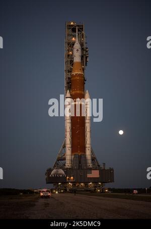 Der Mond steigt hinter der NASA-Rakete Space Launch System (SLS) mit der Orion-Sonde an Bord auf einem mobilen Trägerrakete auf, während er zum ersten Mal am Donnerstag, dem 17. März 2022, im Kennedy Space Center der NASA in Florida zum Launch Complex 39B ausrollt. Vor dem Artemis I-Flugtest der NASA werden die vollständig gestapelte und integrierte SLS-Rakete und die Orion-Raumsonde im Launch Complex 39B einer Nassprobe unterzogen, um die Systeme zu verifizieren und Countdown-Verfahren für den ersten Start zu üben. Stockfoto