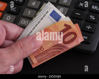 Ein Mann, der Euro-Banknoten in der Hand hält, mit einem Rechner im Hintergrund. Nahaufnahme. Stockfoto