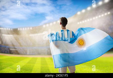 Argentinischer Fußballfan im Stadion. Argentinische Fans auf dem Fußballplatz beobachten das Mannschaftsspiel. Junger Fußballspieler mit Flagge und Nationaltrikot Stockfoto