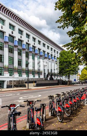 Eine Reihe von Santander mietet Fahrräder, die gegenüber dem berühmten Carreras Art déco-Gebäude in Camden warten.das Gebäude beherbergt heute Hunderte von Büromitarbeitern. Stockfoto